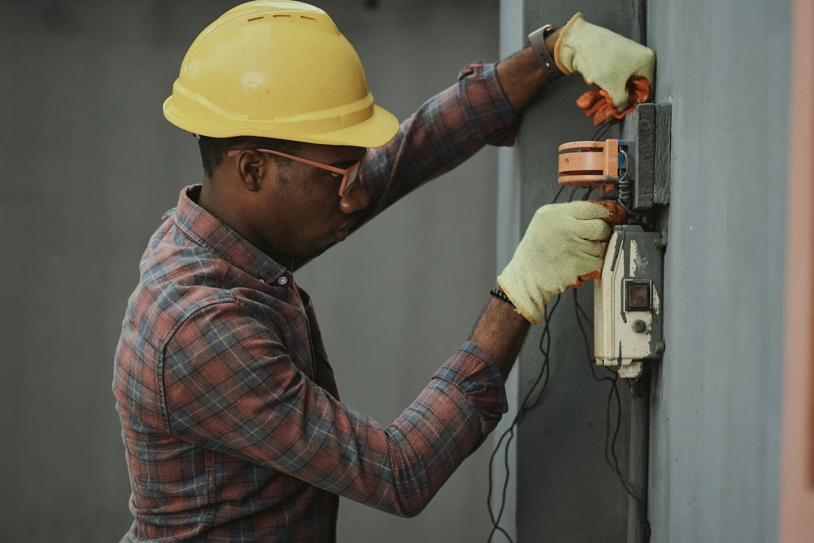 Electrician in a hard hat working at an open electrical service panel.
